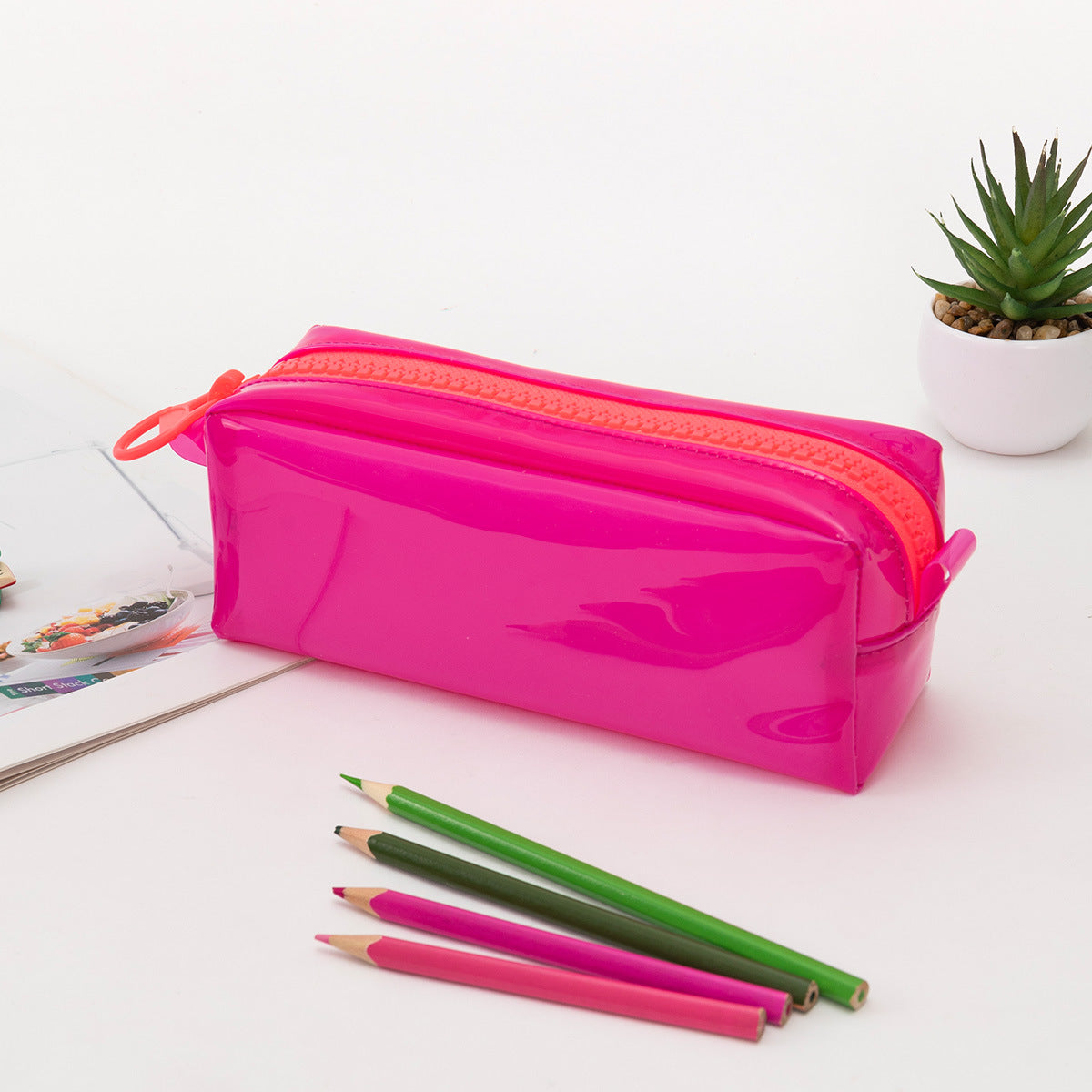 Estuche fucsia de silicona con cremallera naranja, diseño moderno y amplio para útiles escolares o de oficina.