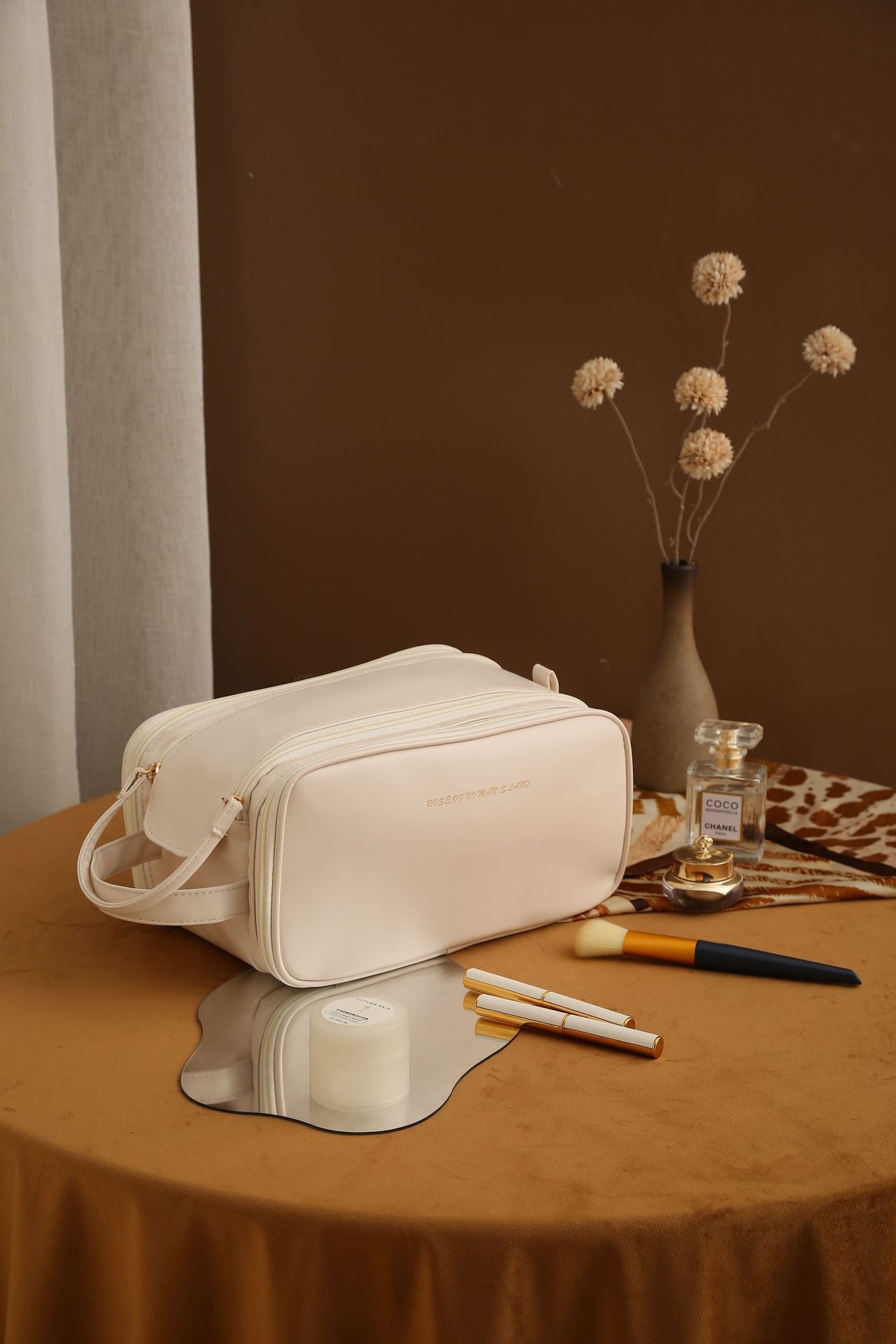 Neceser de maquillaje de PU color crema sobre mesa decorativa, ideal para viajes y almacenamiento de productos de belleza.