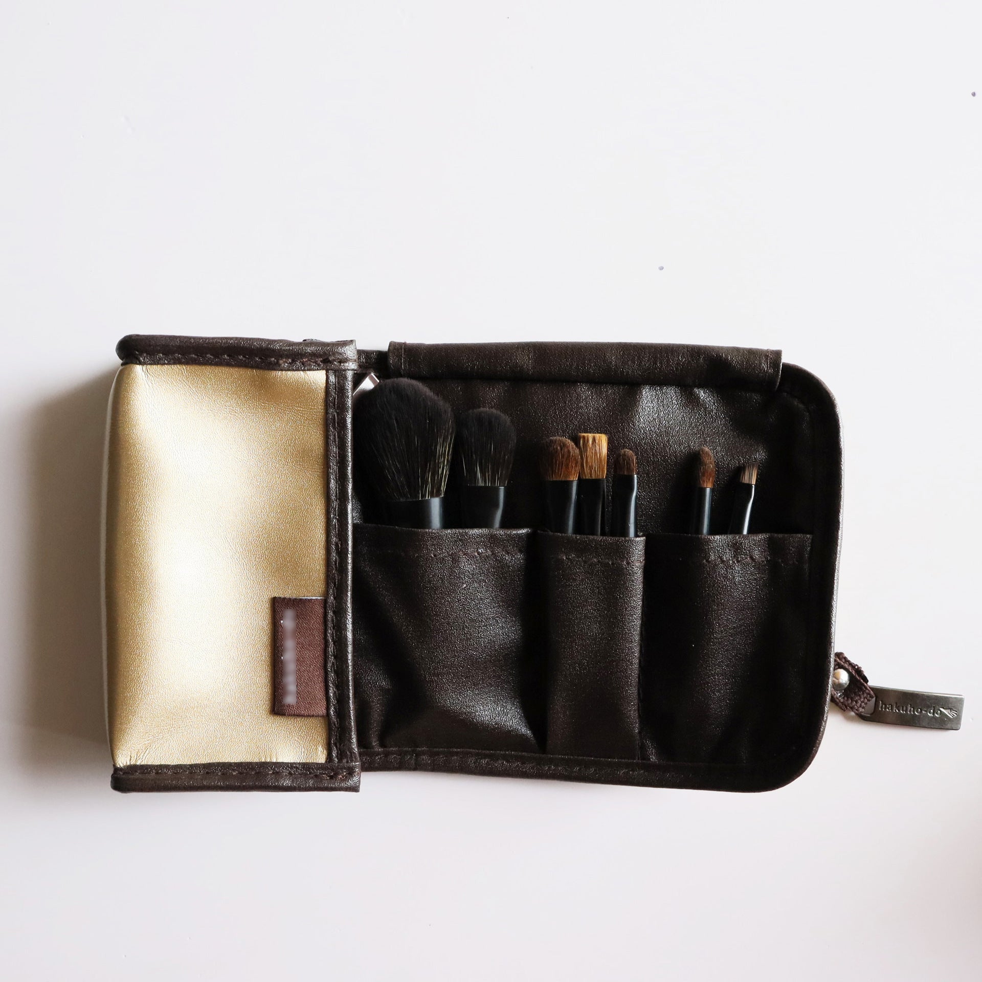 Set compacto de brochas de maquillaje con estuche marrón y dorado, incluye pinceles para sombra, cejas y rostro.